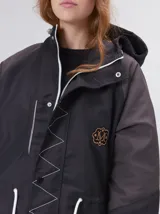 Campera tipo piloto con capucha, cierre frontal con botones y detalle de costuras en zigzag. Presenta cordones ajustables en la cintura y capucha, puños elásticos y logo bordado en el pecho.