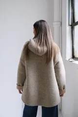 Tapado de paño con capucha, color beige, con cierre frontal, bolsillos laterales y puños vueltos en tono más claro.