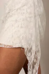 Pollera corta de encaje blanco con diseño asimétrico y volados, estilo pareo.