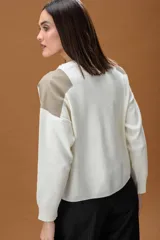 Sweater de punto color beige con cuello redondo y detalles de parches en cuero sintético blanco en los hombros. Presenta mangas largas con puños acanalados y un corte holgado.