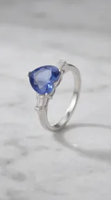 Anillo de plata 925 con piedra central en forma de corazón color azul y detalles laterales de circonias rectangulares tipo baguette.