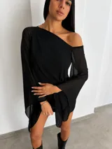 Vestido corto negro de diseño asimétrico con un hombro al descubierto y mangas largas acampanadas de tejido semitransparente.