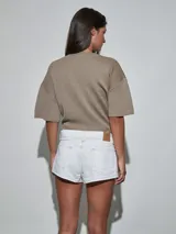 Short de jean blanco con tachas doradas decorativas en los bolsillos delanteros y en los laterales, talle medio y cierre frontal con botón y cremallera.