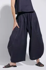 Pantalón azul marino de silueta amplia y voluminosa con diseño redondeado hacia el ruedo. Cuenta con cintura elástica, bolsillos laterales y detalle de tachas metálicas en las costuras laterales.