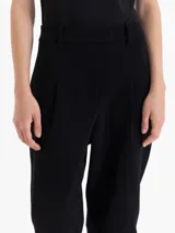 Pantalon negro de corte tipo babucha, con cintura estructurada, presillas para cinturón, bolsillos traseros y ruedos ajustados con puños tejidos.
