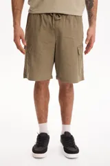 Bermuda cargo color verde militar de corte baggy, con spandex, cintura elastizada y cordón ajustable. Cuenta con bolsillos laterales con solapa en las piernas.