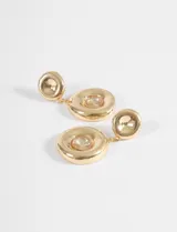 Par de caravanas colgantes doradas con un diseño de doble círculo. El círculo superior es pequeño y liso, mientras que el inferior es más grande, con una forma irregular y un cristal brillante en el centro.