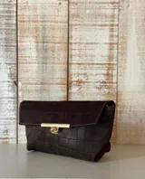 Sobre de mano tipo clutch en color marrón oscuro, con textura efecto cocodrilo y cierre metálico frontal en tono dorado.