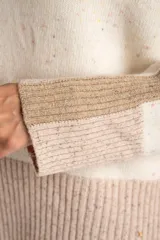 Sweater de lana color crema con efecto tweed, de calce oversize y cuello redondo. Presenta bloques de color en la parte inferior, puños y laterales de las mangas en tono beige con textura acanalada y detalles brillantes.