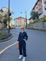 Mono de gabardina negro con cuello camisero, cierre frontal con botones metálicos, mangas largas y bolsillos tipo cargo en el pecho y las piernas. Incluye un cinturón ancho con hebilla del mismo tono para ajustar la cintura.