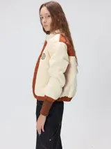 Campera crop de estilo boxy, confeccionada en corderito color crema con paneles acolchados en color terracota en el frente y las mangas. Presenta cuello alto, cierre frontal metálico, puños y ruedo elastizados, y logo de la marca bordado en el pecho.