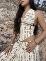 Top de cuello halter con escote en V profundo y bajo en punta. Presenta un diseño de rayas horizontales irregulares en color marrón sobre fondo beige y se ajusta mediante lazos en el cuello y la espalda.