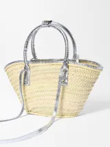 Canasto tejido a mano en fibra vegetal de Jacquemus, modelo Le Petit Panier Soli, con detalles, asas cortas y bolsillo frontal de cuero con acabado metalizado plateado, y logo grabado en letras doradas.