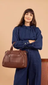 Cartera de mano y hombro color beige, de material símil cuero, con forma estructurada y redondeada. Posee dos asas cortas superiores y una correa larga ajustable y desmontable. Cuenta con un bolsillo exterior con cierre en la parte frontal.