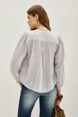 Camisa de algodón color celeste claro, con textura sutil y pequeños bordados blancos en forma de rombos. Presenta cuello mao, botones frontales y mangas largas abullonadas con puños ajustados.