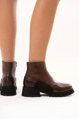 Bota de cuero color chocolate con caña al tobillo y cierre lateral. Presenta una combinación de texturas en el cuero y una suela chunky dentada de color negro.
