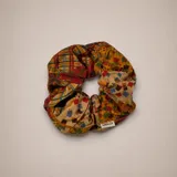 Colero de tela con diseño de patchwork que combina estampados florales, geométricos y de cuadros en tonos cálidos como amarillo, rojo y azul. Cuenta con una etiqueta de la marca Amalfi.