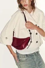 Bolso de hombro de diseño semicircular, confeccionado en material sintético efecto charol de color rojo. Cuenta con una correa ajustable fina con detalles metálicos dorados y cierre superior con cremallera.