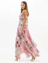 Vestido largo de fiesta con estampado floral en tonos rosa y gris sobre fondo blanco. Presenta cuello halter con abertura tipo lágrima, cintura drapeada y falda amplia con capas asimétricas y bajo en picos. Confeccionado en tejido ligero con forro interior.