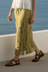 Falda midi color verde oliva con estampado de ramas en negro y blanco. Tiene corte evasé, cintura alta con cordón ajustable y abertura lateral.