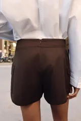 Falda pantalón cruzada de color marrón oscuro, con diseño tipo cargo que incluye bolsillos laterales con solapa y botones decorativos en la cintura.