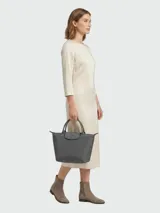 Cartera de mano modelo Le Pliage One de Longchamp, tamaño pequeño, en color gris. Presenta un diseño icónico con solapa de cuero y cierre de botón a presión, cuerpo de material resistente y asas cortas de cuero.