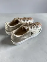Sneakers de cuero dorado con cordones, suela blanca de goma y detalles pintados a mano en la puntera por la artista Carolina De Cunto.