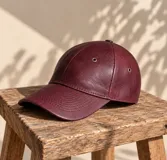 Gorro tipo visera color bordó, confeccionado en 100% cuero, con ojales metálicos de ventilación y costuras decorativas en la visera.