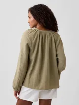 Camisa de muselina color verde militar, de manga larga abullonada, con cuello redondo fruncido y cierre frontal de botones.