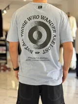 Remera oversize de color celeste con efecto gastado acid wash, mangas cortas y cuello redondo. Cuenta con un gran estampado circular en la espalda con la frase "Not all those who wander are lost" y texto adicional debajo.