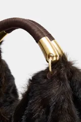 Maxi bolso de mano con acabado de pelo sintético en color marrón oscuro. Presenta un diseño estructurado con doble asa de mano reforzada y detalles metálicos dorados en las uniones. Cuenta con cierre mediante botón imantado y forro interior con bolsillo con cremallera.
