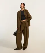 Pantalón de sastrería corte barrel, color verde militar, con cintura de tiro medio, cierre desplazado, pliegues frontales y piernas anchas.