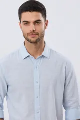 Camisa de manga larga confeccionada en mezcla de lino y algodón, con sutiles rayas celestes, cuello camisero clásico y cierre frontal de botones.