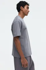Remera gris de corte relajado, confeccionada en punto liviano con cuello redondo ribeteado, hombros caídos y mangas cortas.