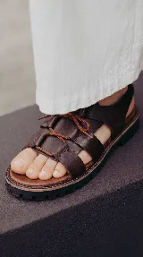 Sandalia de cuero color visón con tiras anchas entrelazadas, cordones ajustables en el empeine, suela dentada y base de goma.