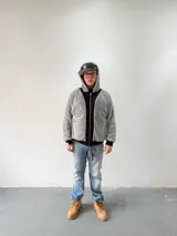 Campera reversible con cierre frontal, diseño oversize. Un lado es de algodón negro con estampados y bordados gráficos, mientras que el otro lado es de tela polar gris de pelo largo. Cuenta con capucha, puños y ruedo acanalados.