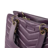 Cartera de mano color púrpura, con diseño acolchado en símil cuero soft y costuras a tono. Tiene acceso con cierre y broches imantados, herrajes dorados y correa regulable para usar como bandolera. El interior está forrado en tela de algodón y poliéster, con un bolsillo con cierre y dos abiertos.