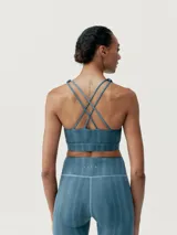 Top deportivo de sujeción media, color azul con diseño de líneas verticales en degradé. Tiene tirantes finos dobles cruzados en la espalda y logo en el frente.