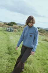 Sweater de tejido de punto en color azul, con cuello alto y calce relajado. Presenta detalles bordados en contraste en el cuello, puños y ruedo, además de un bolsillo frontal con un aplique en forma de corazón.