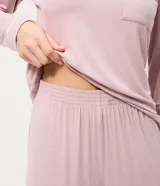 Pijama de dos piezas compuesto por una blusa de manga larga con cuello redondo y bolsillo frontal, y un pantalón recto con cintura elástica. Ambas prendas presentan detalles de piping en los bordes. Confeccionado en tejido de viscolycra suave y fluido.