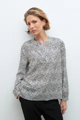 Blusa beige con estampado de lunares negros, cuello en V y mangas largas.