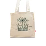 Bolso tipo tote color crudo con estampa de paisaje de playa con palmera, sombrilla, tabla de surf y gaviotas.