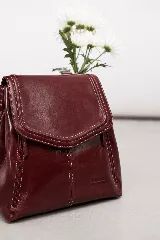 Mochila de cuero vacuno marrón con acabado pulido, solapa en forma de V y costuras decorativas. Cuenta con cremalleras laterales y asas ajustables.