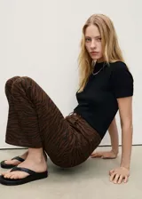 Pantalón de jean con diseño recto y tiro alto, confeccionado en algodón con estampado animal print de cebra en tonos marrones. Cuenta con cierre frontal de cremallera y botón, trabillas para cinturón y cinco bolsillos clásicos.