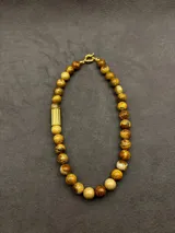 Collar de cuentas de piedras naturales en tonos tierra, con detalles de tubos dorados en los laterales.