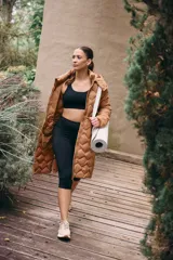 Campera larga color marrón con diseño acolchado, capucha desmontable, cierre frontal con botones a presión, bolsillos laterales con cierre, puños elásticos y cintura ajustable.