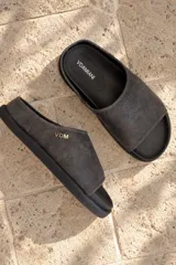 Sandalia tipo clog Vdamiani modelo Dune, confeccionada en cuero gastado color gris oscuro, con suela plana y mini plataforma. Cuenta con detalles de costuras y las iniciales de la marca en herraje metálico dorado en el lateral.