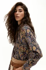 Camisa de algodón con estampado paisley en tonos azules, naranjas y amarillos. Presenta cuello camisero, mangas largas, botones de nácar en el frente y ruedo curvo, más largo en la parte trasera.