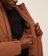 Campera tipo parka color marrón, con capucha ajustable, cierre frontal de cremallera y botones, y múltiples bolsillos con solapa en el frente. Presenta puños ajustables con botones y un diseño funcional de estilo urbano.