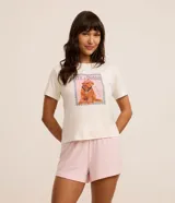 Conjunto de pijama short doll con remera blanca de cuello redondo y manga corta con estampado de un caniche con accesorios y short rosa con lunares blancos.